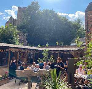 Image shows the beer garden of The Tamworth Tap, packed with drinkers enjoying a pint in the sunshine as Tamworth Castle towers over them